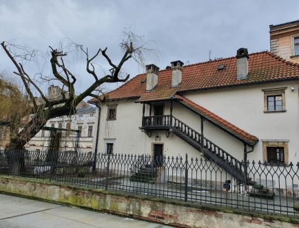 Kolorowa fotografia przedstawiająca budynek Domu Pod Krzyżem wraz z najbliższym otoczeniem.