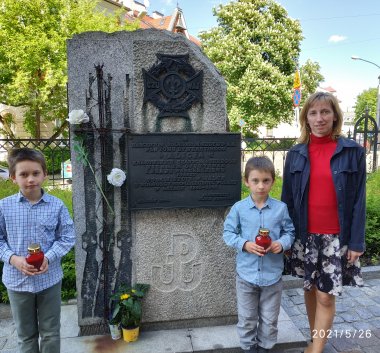 Kolorowa fotografia. Kobieta i dwójka dzieci stojąca przy pomniku